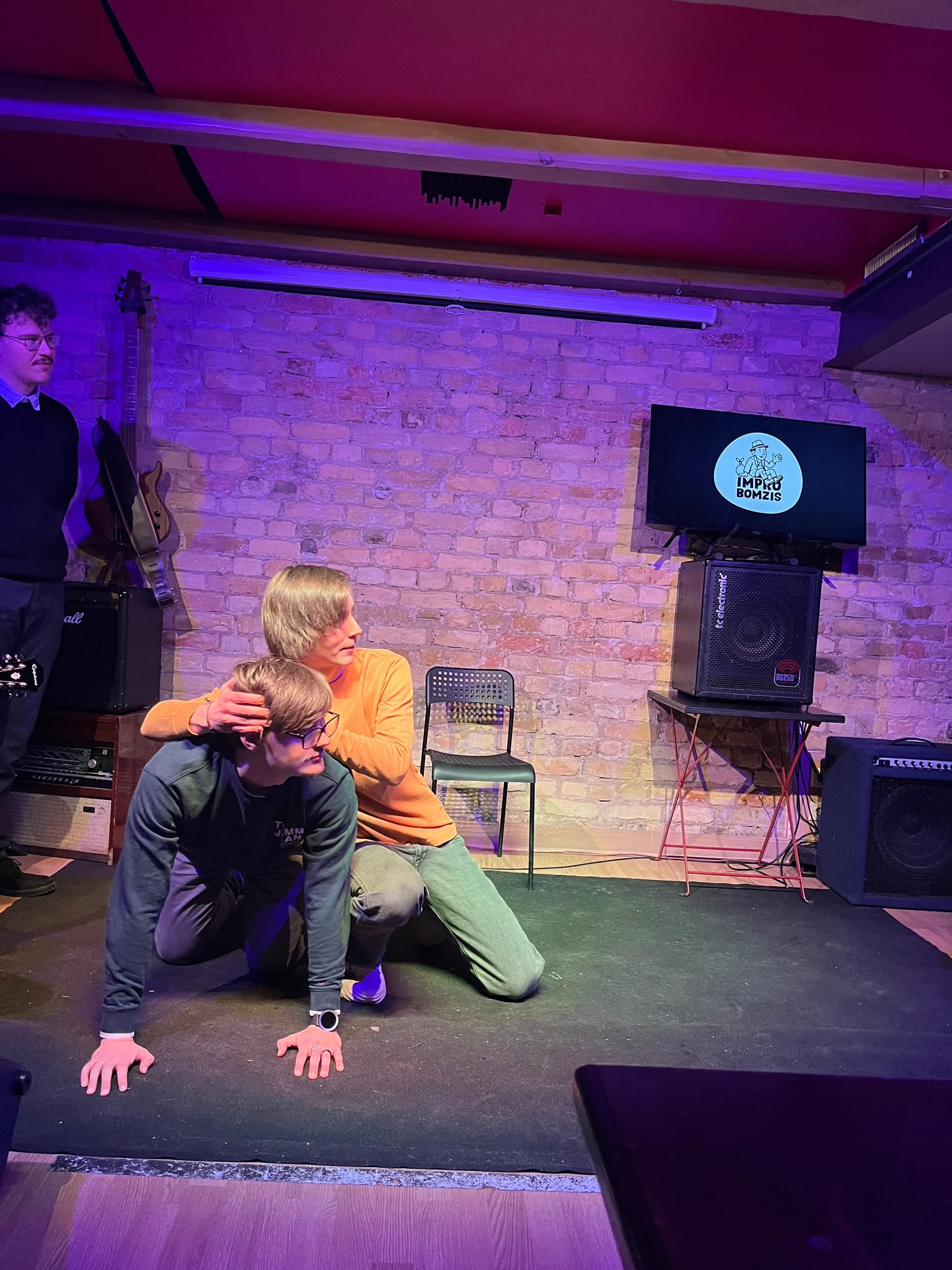 Two performers low on the stage floor in front of a brick wall
