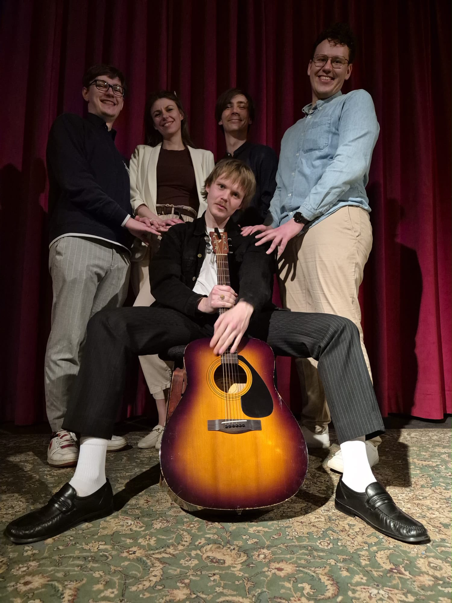 The team posing together on stage around a guitar